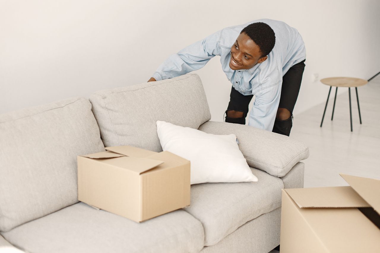 about-02 Young man smiling while arranging cardboard boxes in a modern living room.